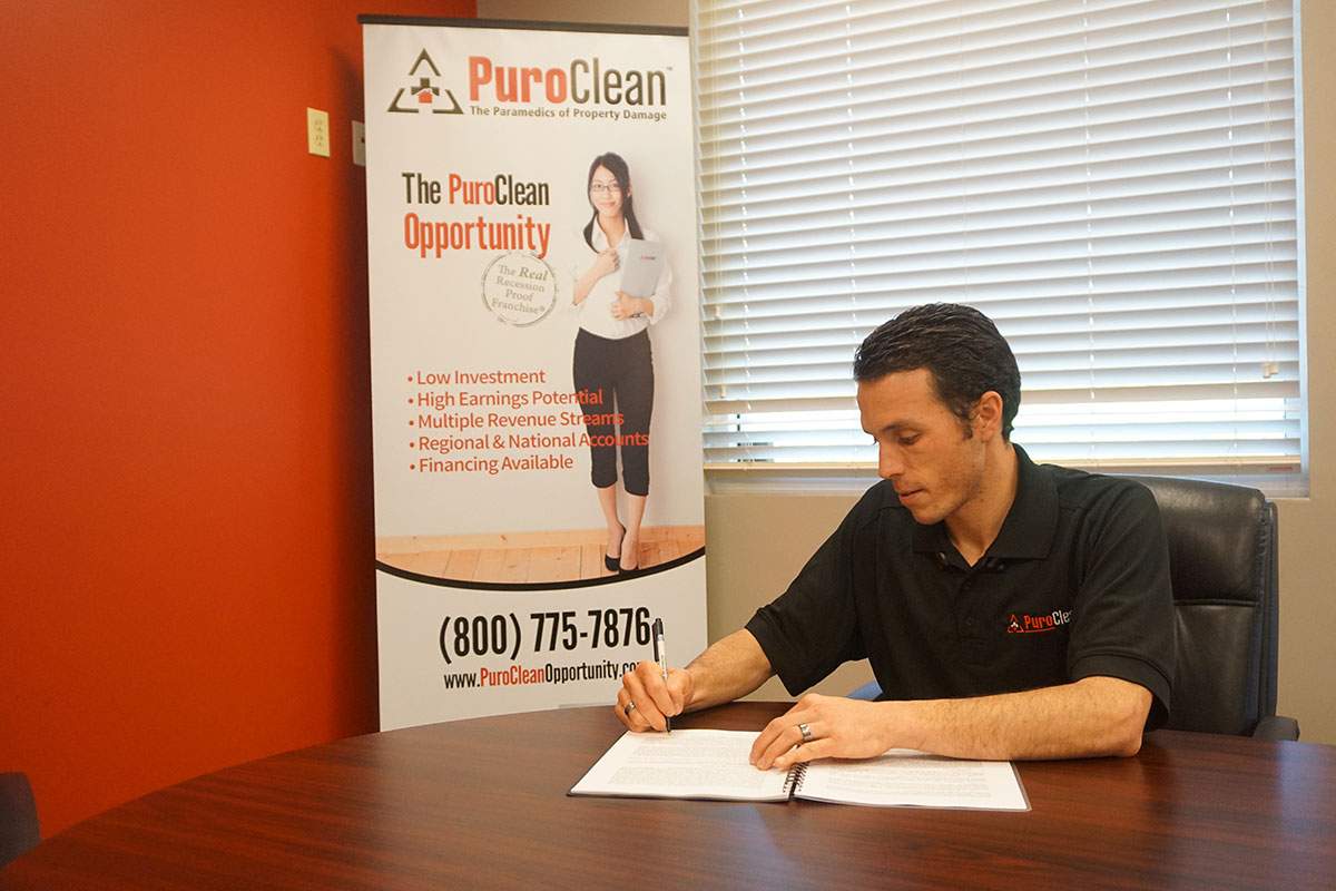 PuroClean franchisee signing paperwork at a desk