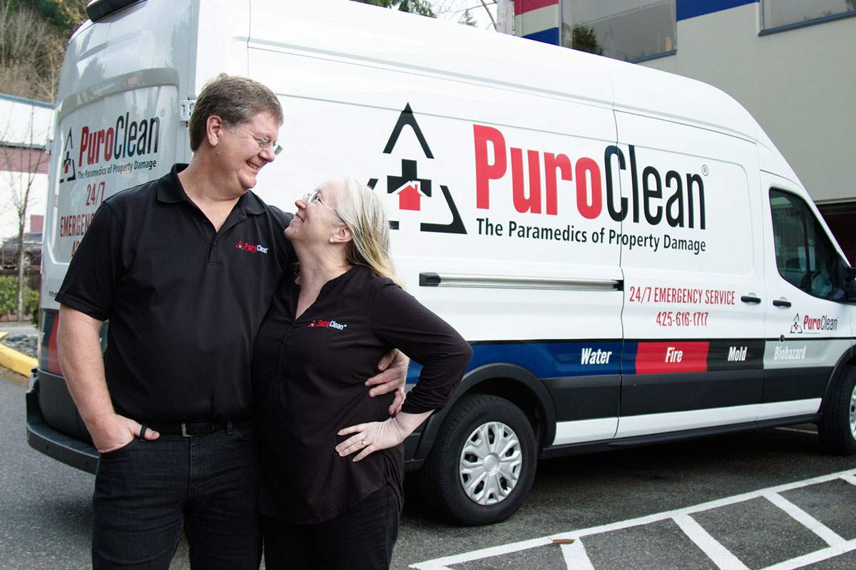 PuroClean franchisee couple standing with a company van