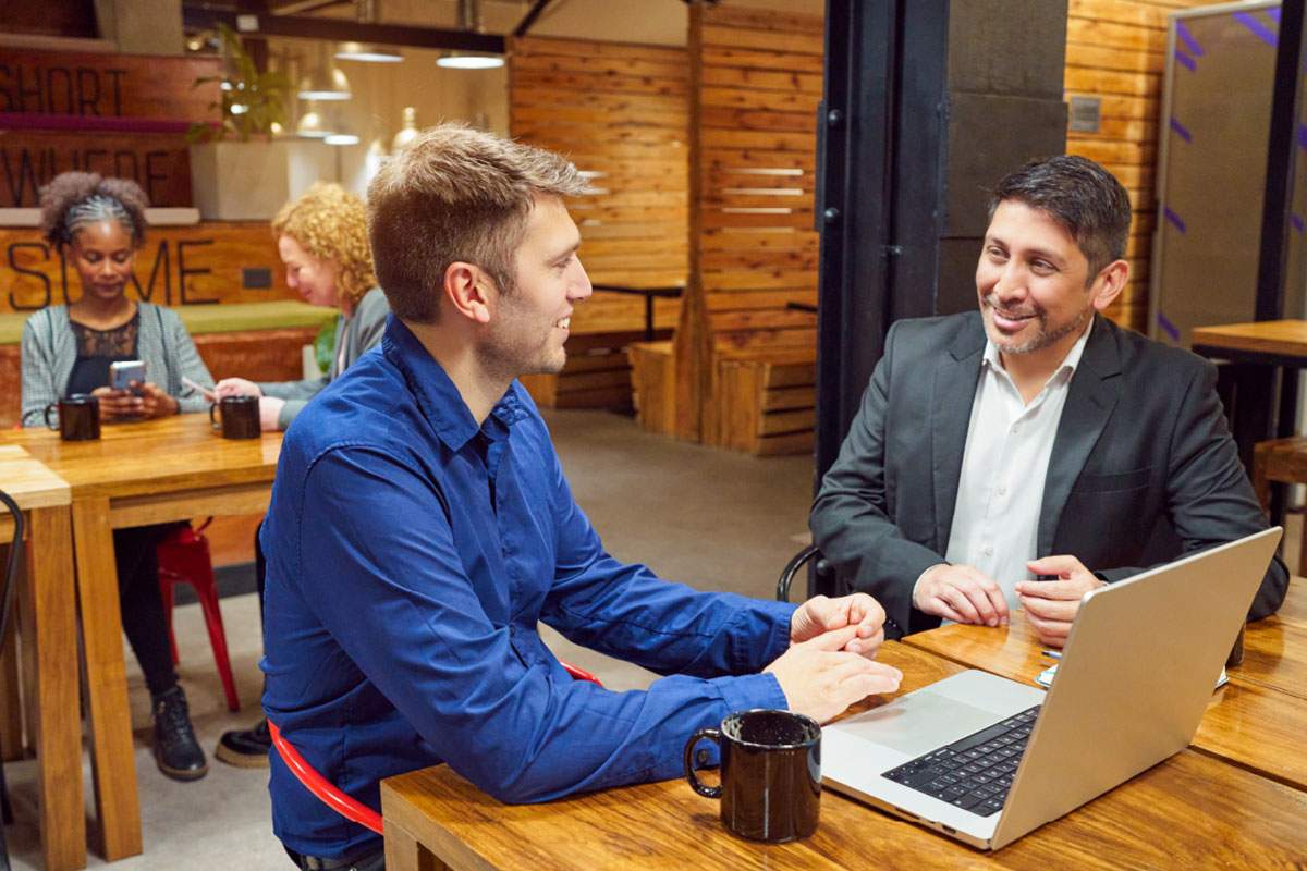 two men at a desk with a laptop out