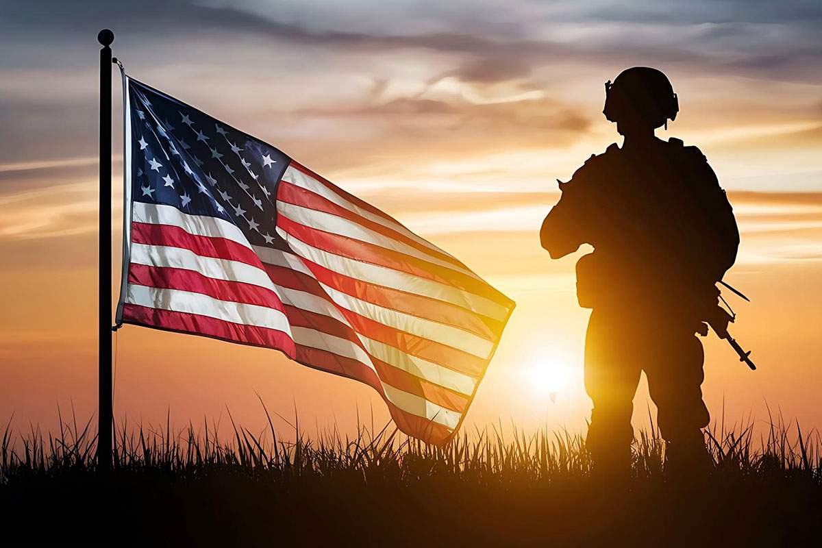 Military personnel stands near American flag at sunset.