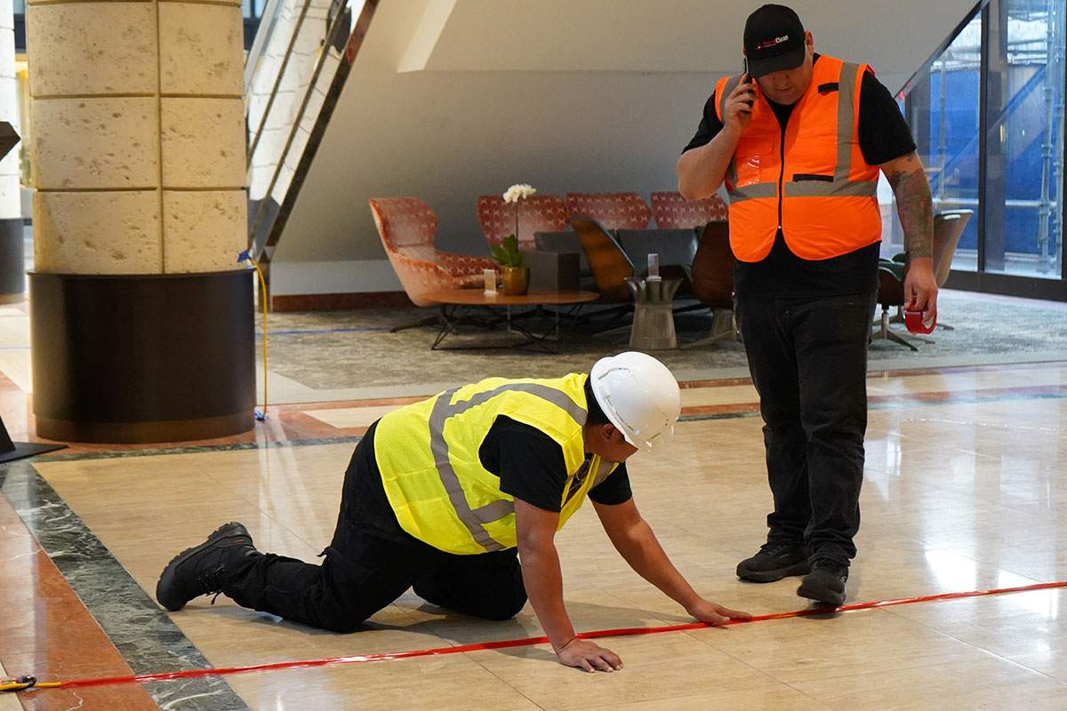 Two men in safety vests are working on the floor