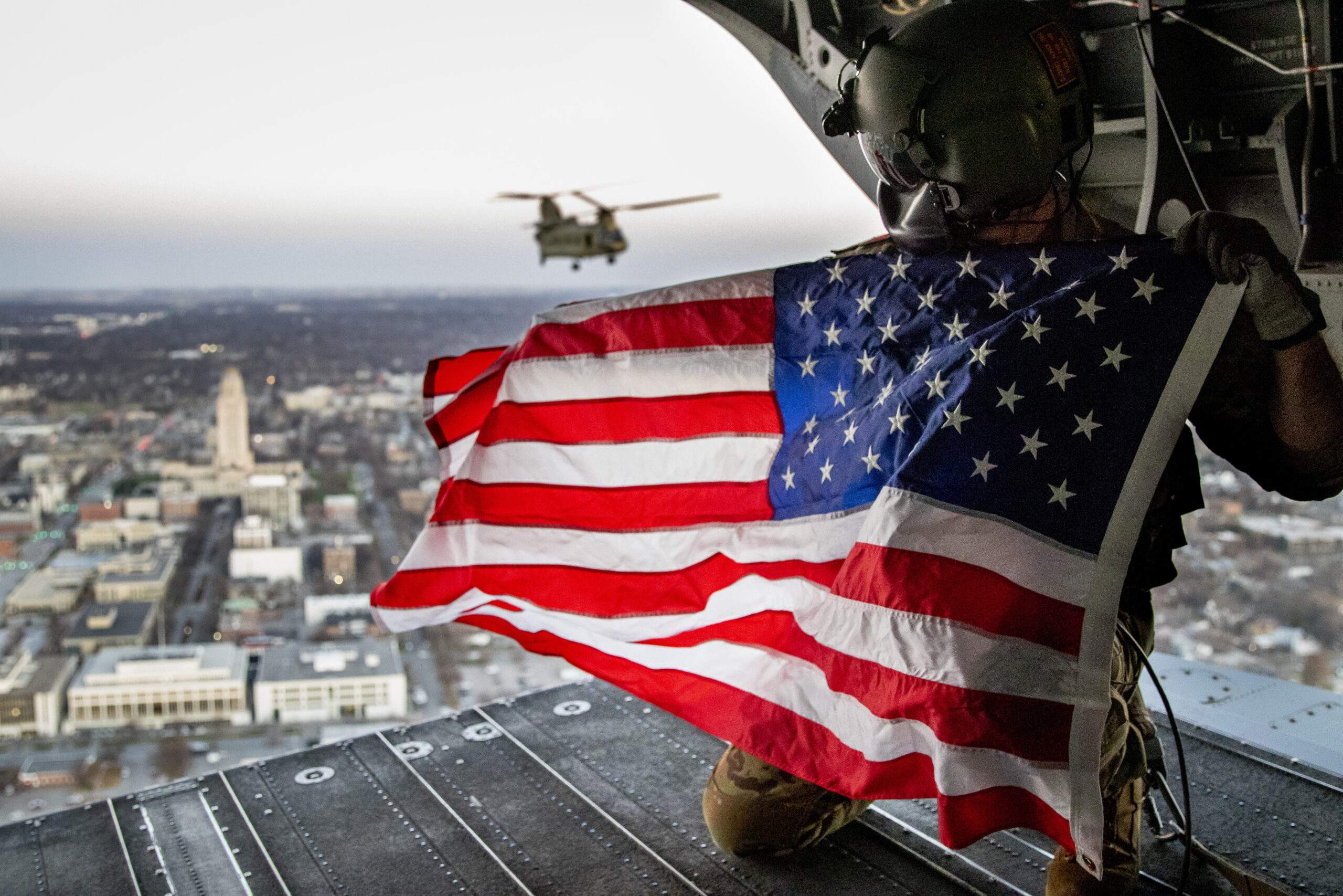 US soldier on the deck of in-air helicopter holding American flag