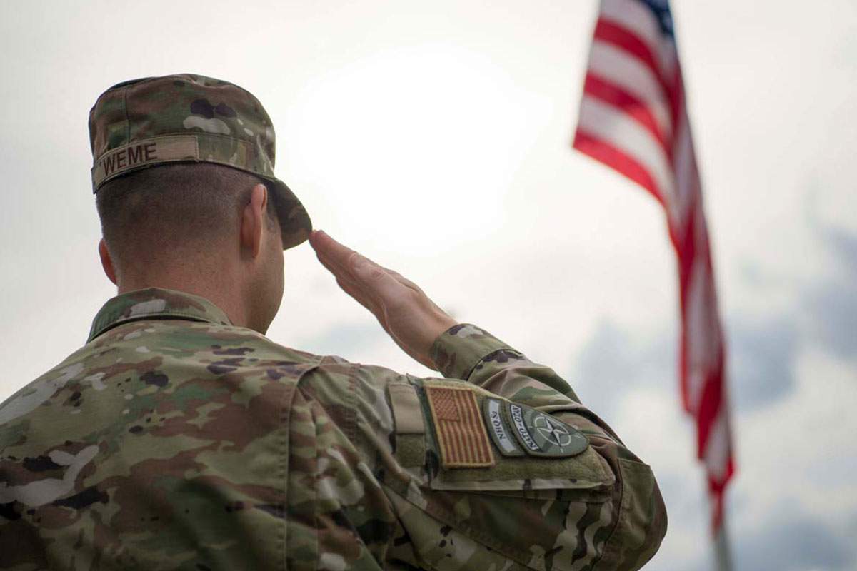 A military service member salutes the American flag.